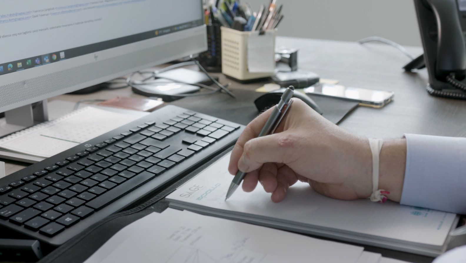 Person writing on a piece of paper in front of a computer